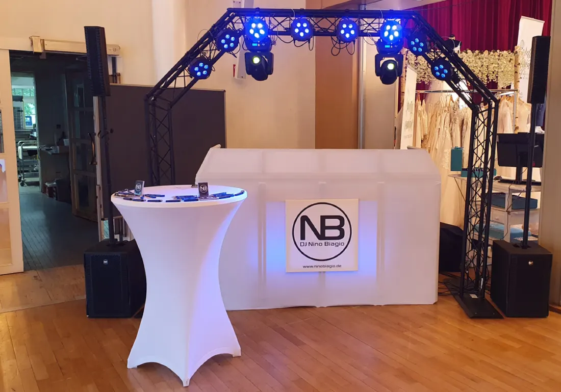 DJ-Aufbau von Nino Biagio mit Traversenbogen, Movingheads und weißem DJ-Pult mit Logo